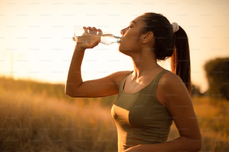 A woman drinking from a glass bottle at sunset
